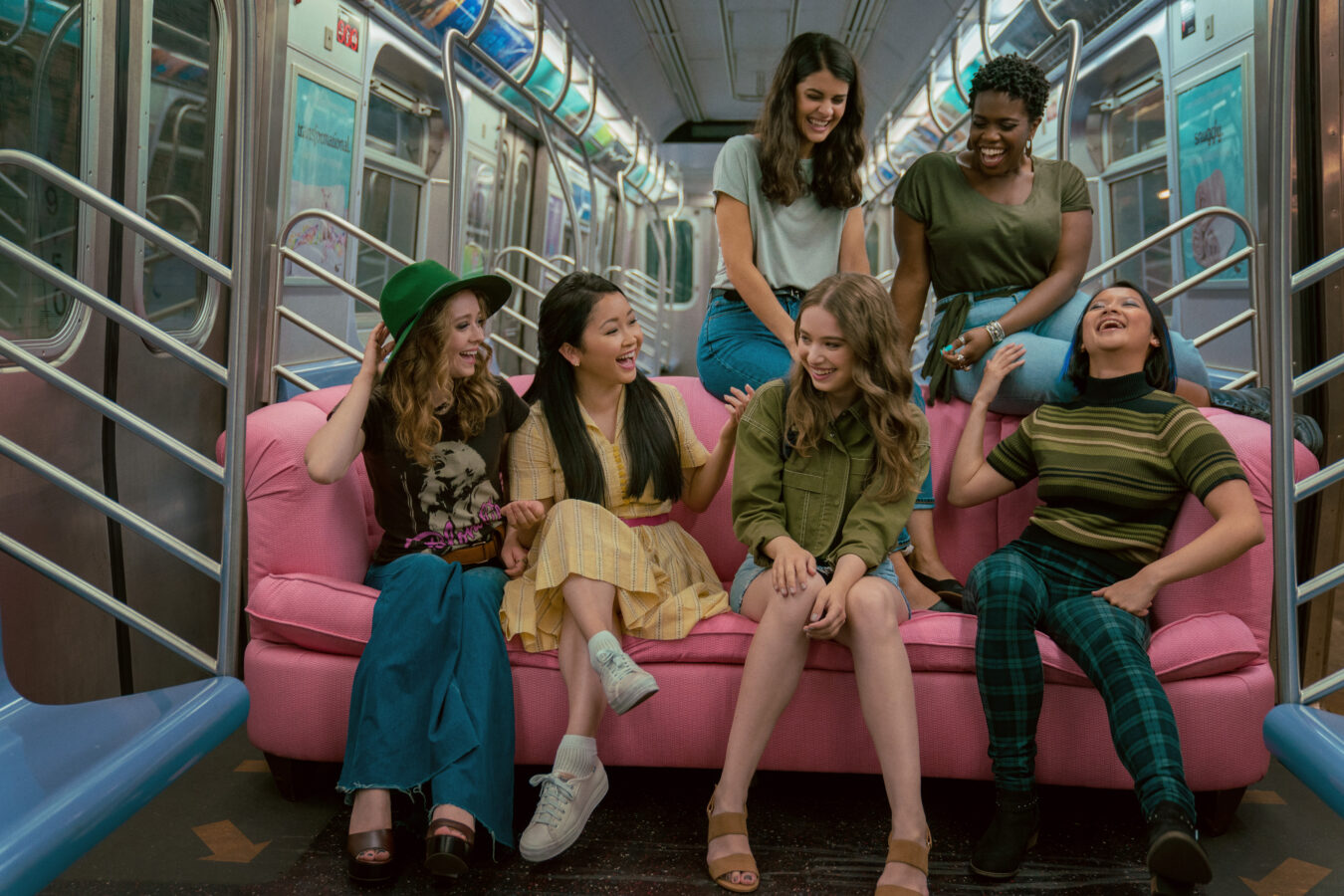 Lara Jean and friends on a pink couch in the NYC subway in To All the Boys 3.